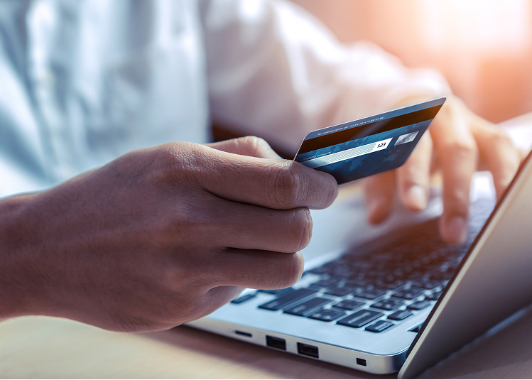 Person holding a credit card while using a laptop, representing CareCredit financing for dermatology procedures.